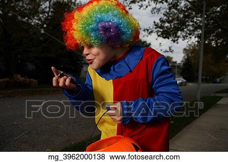 A young boy on the sidewalk on the quest for more halloween candy. He is dressed in a yellow, red and blue clown costume accompanied with a rainbow wig. He is holding a pumpkin filled with candy. © Retna Digital / Retna Ltd. View Large Photo Image Stock Photo - A young boy on the sidewalk on the quest for more halloween candy. He is dressed in a yellow, red and blue clown costume accompanied with a rainbow wig. He is holding a pumpkin filled with candy. © Retna Digital / Retna Ltd.. Fotosearch