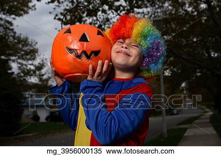 A young boy on the sidewalk on the quest for more halloween candy. He is dressed in a yellow, red and blue clown costume accompanied with a rainbow wig. He is holding a pumpkin filled with candy. © Retna Digital / Retna Ltd. View Large Photo Image Stock Photography - A young boy on the sidewalk on the quest for more halloween candy. He is dressed in a yellow, red and blue clown costume accompanied with a rainbow wig. He is holding a pumpkin filled with candy. © Retna Digital / Retna Ltd.. Fotosearch