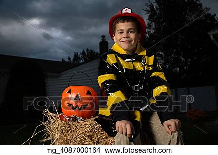 A young boy out on halloween. He is wearing a fireman costume, equipped with hat & coat. He's outside sitting on a haystack with his pumpkin filled with candy. © Retna Digital / Retna Ltd. View Large Photo Image Picture - A young boy out on halloween. He is wearing a fireman costume, equipped with hat & coat. He's outside sitting on a haystack with his pumpkin filled with candy. © Retna Digital / Retna Ltd.. Fotosearch