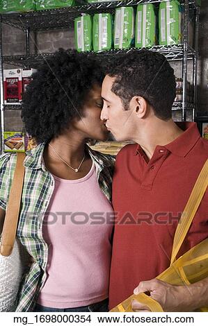 Picture - A young couple embraces while picking out groceries in a store. credit - RD / Retna Digital. Fotosearch