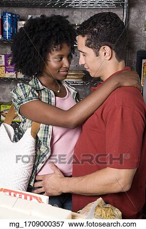 A young couple embraces while picking out groceries in a store. credit - RD / Retna Digital View Large Photo Image Stock Photo - A young couple embraces while picking out groceries in a store. credit - RD / Retna Digital. Fotosearch