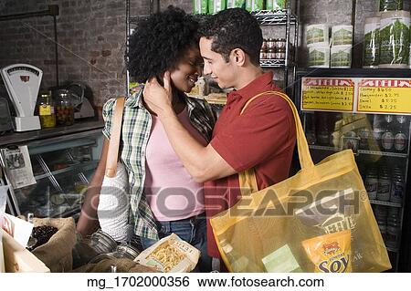 A young couple embraces while picking out groceries in a store. credit - RD / Retna Digital View Large Photo Image Stock Photograph - A young couple embraces while picking out groceries in a store. credit - RD / Retna Digital. Fotosearch