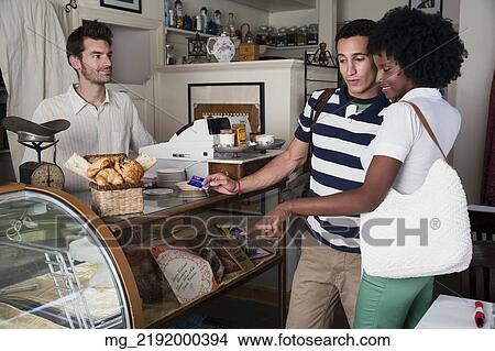 A young couple in their 20's or early 30's buy pastries at a bakery from a man behind a counter. September 1, 2006 credit - RD / Retna Digital View Large Photo Image Picture - A young couple in their 20's or early 30's buy pastries at a bakery from a man behind a counter. September 1, 2006 credit - RD / Retna Digital. Fotosearch