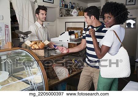 A young couple in their 20's or early 30's buy pastries at a bakery from a man behind a counter. September 1, 2006 credit - RD / Retna Digital View Large Photo Image Stock Photo - A young couple in their 20's or early 30's buy pastries at a bakery from a man behind a counter. September 1, 2006 credit - RD / Retna Digital. Fotosearch