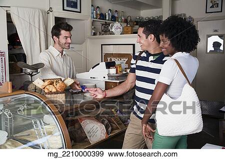 A young couple in their 20's or early 30's buy pastries at a bakery from a man behind a counter. September 1, 2006 credit - RD / Retna Digital View Large Photo Image Stock Photo - A young couple in their 20's or early 30's buy pastries at a bakery from a man behind a counter. September 1, 2006 credit - RD / Retna Digital. Fotosearch