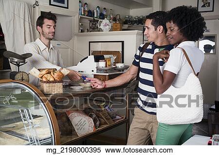 Stock Photography - A young couple in their 20's or early 30's buy pastries at a bakery from a man behind a counter. September 1, 2006 credit - RD / Retna Digital. Fotosearch