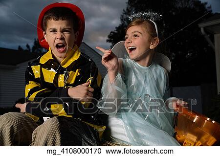 Stock Image - A young girl & boy out on halloween. He is wearing a fireman costume, equipped with hat & coat. The Girl is dressed as a fairy princess in a light blue gown, wings and a halo. They are outside sitting on a haystack playing. © Retna Digital / Retna Lt. Fotosearch