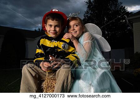 A young girl & boy out on halloween. He is wearing a fireman costume, equipped with hat & coat. The Girl is dressed as a fairy princess in a light blue gown, wings and a halo. They are outside sitting on a haystack playing. © Retna Digital / Retna Lt View Large Photo Image Stock Image - A young girl & boy out on halloween. He is wearing a fireman costume, equipped with hat & coat. The Girl is dressed as a fairy princess in a light blue gown, wings and a halo. They are outside sitting on a haystack playing. © Retna Digital / Retna Lt. Fotosearch