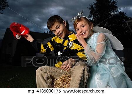 A young girl & boy out on halloween. He is wearing a fireman costume, equipped with hat & coat. The Girl is dressed as a fairy princess in a light blue gown, wings and a halo. They are outside sitting on a haystack playing. © Retna Digital / Retna Lt View Large Photo Image Stock Photography - A young girl & boy out on halloween. He is wearing a fireman costume, equipped with hat & coat. The Girl is dressed as a fairy princess in a light blue gown, wings and a halo. They are outside sitting on a haystack playing. © Retna Digital / Retna Lt. Fotosearch