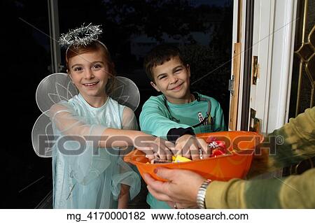 Stock Image - A young girl & boy out on halloween. She is dressed as a fairy princess in a light blue gown, wings and a halo. The boy is wearing O. R. scrubs. They are in a doorway getting thier candy treats. © Retna Digital / Retna Ltd.. Fotosearch