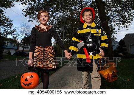 Stock Photograph - A young girl & boy walking down the sidewalk on a quest for more halloween candy. She is dressed as a cat in a black unitard and tights with a animal print fur trim collar and skirt. She uses makeup to a cat noses and whiskers and costume ears. The Boy. Fotosearch