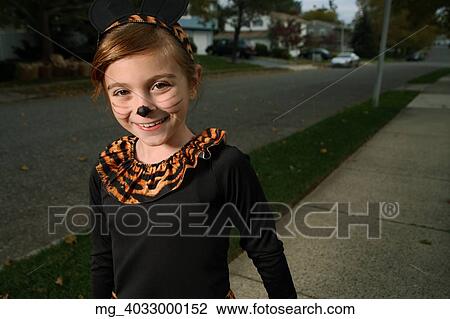 Stock Image - A young girl on the sidewalk on the quest for more halloween candy. She is dressed as a cat in a black unitard and tights with a animal print fur trim collar. She uses makeup to a cat noses and whiskers and costume ears. © Retna Digital / Retna Ltd.. Fotosearch