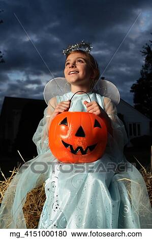 A young girl out on halloween. She is dressed as a fairy princess in a light blue gown, wings and a halo. She is sitting outside on a haystack with a pumpkin filled with candy. © Retna Digital / Retna Ltd. View Large Photo Image Stock Image - A young girl out on halloween. She is dressed as a fairy princess in a light blue gown, wings and a halo. She is sitting outside on a haystack with a pumpkin filled with candy. © Retna Digital / Retna Ltd.. Fotosearch