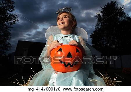 A young girl out on halloween. She is dressed as a fairy princess in a light blue gown, wings and a halo. She is sitting outside on a haystack with a pumpkin filled with candy. © Retna Digital / Retna Ltd. View Large Photo Image Stock Photo - A young girl out on halloween. She is dressed as a fairy princess in a light blue gown, wings and a halo. She is sitting outside on a haystack with a pumpkin filled with candy. © Retna Digital / Retna Ltd.. Fotosearch