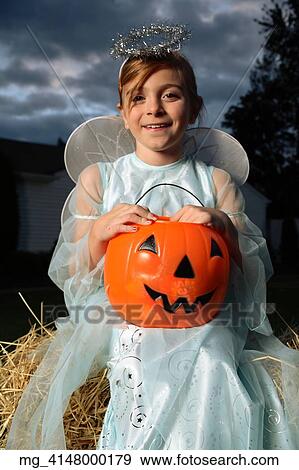 A young girl out on halloween. She is dressed as a fairy princess in a light blue gown, wings and a halo. She is sitting outside on a haystack with a pumpkin filled with candy. © Retna Digital / Retna Ltd. View Large Photo Image Stock Photo - A young girl out on halloween. She is dressed as a fairy princess in a light blue gown, wings and a halo. She is sitting outside on a haystack with a pumpkin filled with candy. © Retna Digital / Retna Ltd.. Fotosearch