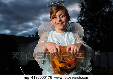 A young girl out on halloween. She is dressed as a fairy princess in a light blue gown, wings and a halo. She is sitting outside on a haystack with a pumpkin filled with candy. © Retna Digital / Retna Ltd. View Large Photo Image Stock Photograph - A young girl out on halloween. She is dressed as a fairy princess in a light blue gown, wings and a halo. She is sitting outside on a haystack with a pumpkin filled with candy. © Retna Digital / Retna Ltd.. Fotosearch