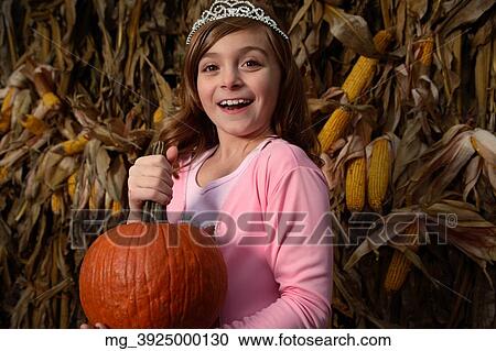 A young girl outside in the middle of a corn field on halloween dressed in a pink flowing princess dress and tiara crown. She's holding a pumpkin by the stem. © Retna Digital / Retna Ltd. View Large Photo Image Stock Image - A young girl outside in the middle of a corn field on halloween dressed in a pink flowing princess dress and tiara crown. She's holding a pumpkin by the stem. © Retna Digital / Retna Ltd.. Fotosearch