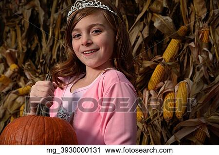 A young girl outside in the middle of a corn field on halloween dressed in a pink flowing princess dress and tiara crown. She's holding a pumpkin by the stem. © Retna Digital / Retna Ltd. View Large Photo Image Stock Image - A young girl outside in the middle of a corn field on halloween dressed in a pink flowing princess dress and tiara crown. She's holding a pumpkin by the stem. © Retna Digital / Retna Ltd.. Fotosearch