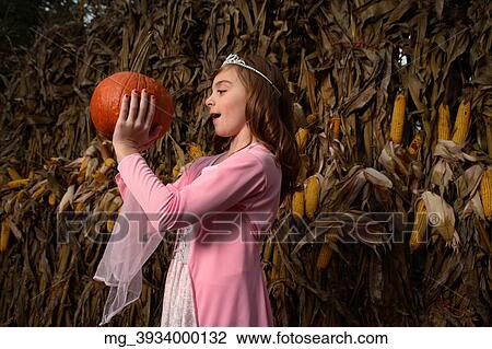 A young girl outside in the middle of a corn field on halloween dressed in a pink flowing princess dress and tiara crown. She's holding a pumpkin by the stem. © Retna Digital / Retna Ltd. View Large Photo Image Stock Image - A young girl outside in the middle of a corn field on halloween dressed in a pink flowing princess dress and tiara crown. She's holding a pumpkin by the stem. © Retna Digital / Retna Ltd.. Fotosearch