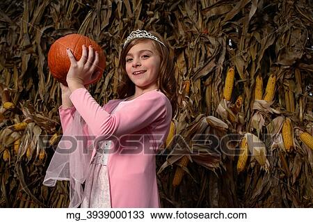 A young girl outside in the middle of a corn field on halloween dressed in a pink flowing princess dress and tiara crown. She's holding a pumpkin by the stem. © Retna Digital / Retna Ltd. View Large Photo Image Stock Image - A young girl outside in the middle of a corn field on halloween dressed in a pink flowing princess dress and tiara crown. She's holding a pumpkin by the stem. © Retna Digital / Retna Ltd.. Fotosearch