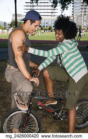 Stock Image - A young man and a young woman on a bike both in their 20's meet in the park and talk. September 1, 2006 credit - RD / Retna Digital. Fotosearch
