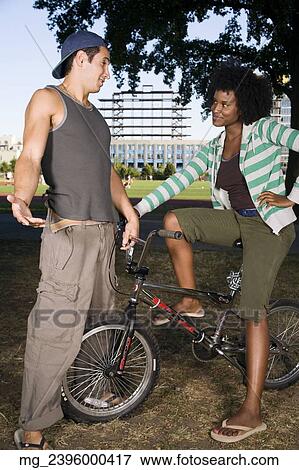 Stock Photo - A young man and a young woman on a bike both in their 20's meet in the park and talk. September 1, 2006 credit - RD / Retna Digital. Fotosearch