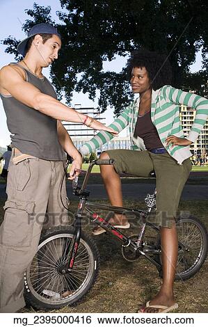 Stock Photograph - A young man and a young woman on a bike both in their 20's meet in the park and talk. September 1, 2006 credit - RD / Retna Digital. Fotosearch