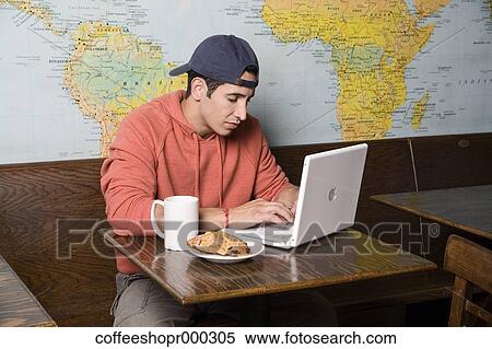 A young man enjoys a drink at a coffee shop while on his computer. December 30, 2006 credit - RD / Retna Digital View Large Photo Image Stock Photography - A young man enjoys a drink at a coffee shop while on his computer. December 30, 2006 credit - RD / Retna Digital. Fotosearch