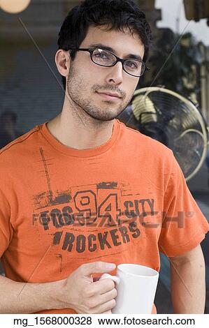 A young man in glasses, orange shirt and blue jeans outside a shop while enjoying a drink. September 1, 2006 credit - RD / Retna Digital View Large Photo Image Stock Photo - A young man in glasses, orange shirt and blue jeans outside a shop while enjoying a drink. September 1, 2006 credit - RD / Retna Digital. Fotosearch