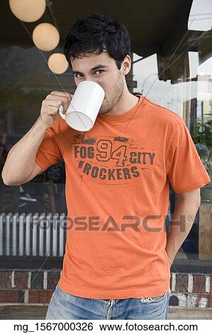 A young man in glasses, orange shirt and blue jeans outside a shop while enjoying a drink. September 1, 2006 credit - RD / Retna Digital View Large Photo Image Stock Photograph - A young man in glasses, orange shirt and blue jeans outside a shop while enjoying a drink. September 1, 2006 credit - RD / Retna Digital. Fotosearch