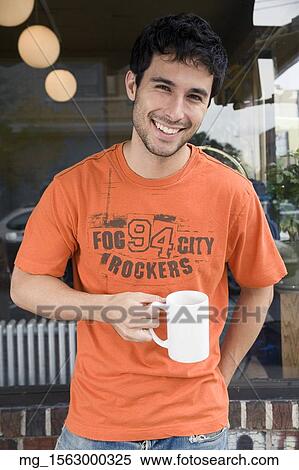 A young man in glasses, orange shirt and blue jeans outside a shop while enjoying a drink. September 1, 2006 credit - RD / Retna Digital View Large Photo Image Stock Photography - A young man in glasses, orange shirt and blue jeans outside a shop while enjoying a drink. September 1, 2006 credit - RD / Retna Digital. Fotosearch