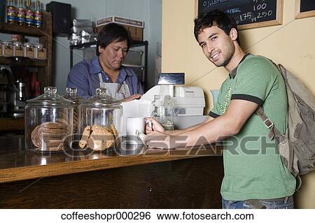 A young man wearing a backpack buys a drink from a coffee shop. December 30, 2006 credit - RD / Retna Digital View Large Photo Image Stock Photograph - A young man wearing a backpack buys a drink from a coffee shop. December 30, 2006 credit - RD / Retna Digital. Fotosearch