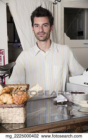 Stock Image - A young man with a beard waits behind the counter of a baery or coffee shop. September 1, 2006 credit - RD / Retna Digital. Fotosearch