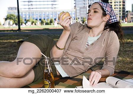 Stock Photo - A young woman in her 20's relaxes while reading a magazine and eating a snack in the park. September 1, 2006 credit - RD / Retna Digital. Fotosearch