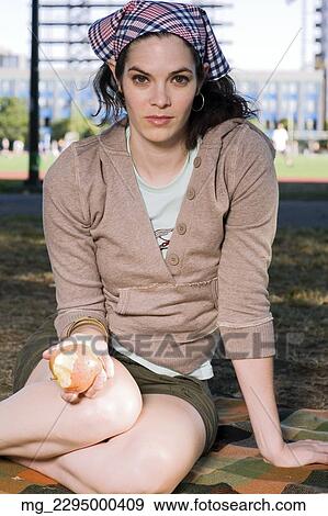 Stock Photo - A young woman in her 20's relaxes while reading a magazine and eating a snack in the park. September 1, 2006 credit - RD / Retna Digital. Fotosearch