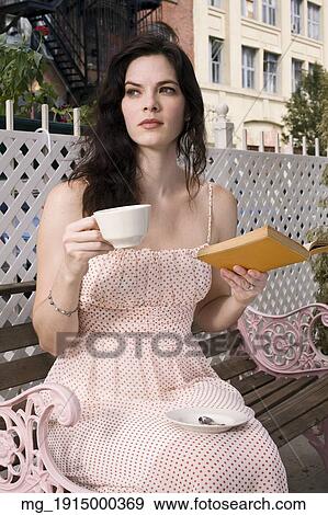 Brunette woman in her 20's wearing a strapless pink dress sits outdoors on a bench drinking a beverage from a mug and reading a book. September 1, 2006. © RD / Retna Digital View Large Photo Image Stock Photo - Brunette woman in her 20's wearing a strapless pink dress sits outdoors on a bench drinking a beverage from a mug and reading a book. September 1, 2006. © RD / Retna Digital. Fotosearch