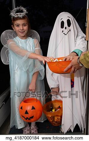 Children out on halloween. The girl is dressed as a fairy princess in a light blue gown, wings and a halo. The other child is dressed as a ghost. They are in a doorway getting thier candy treats. © Retna Digital / Retna Ltd. View Large Photo Image Picture - Children out on halloween. The girl is dressed as a fairy princess in a light blue gown, wings and a halo. The other child is dressed as a ghost. They are in a doorway getting thier candy treats. © Retna Digital / Retna Ltd.. Fotosearch