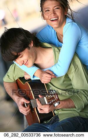 Stock Photograph - Front view waist woman looking at camera embracing a man playing guitar. Fotosearch