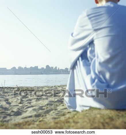 Stock Image - person, human, from behind, sitting, beach, sandy beach. Fotosearch