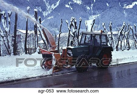 Stock Image - Clearing Snow off a Road using a Tractor Austria. Fotosearch