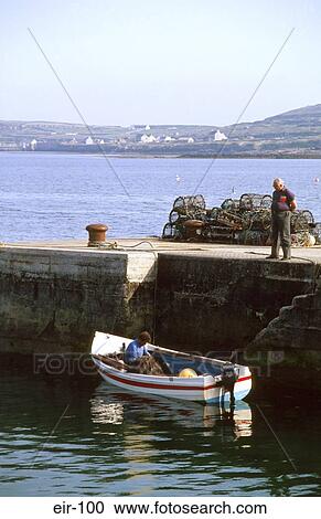 Stock Image - Man on Harbour Wall Looking At Fisherman In Boat. Fotosearch