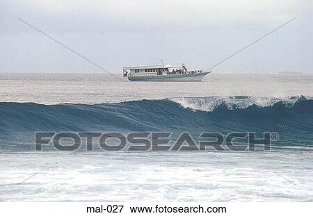 Stock Photo - Breaking Waves and Boat Maldives. Fotosearch