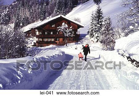 Stock Image - Child on Sledge and Woman Walking in Snow Austria. Fotosearch