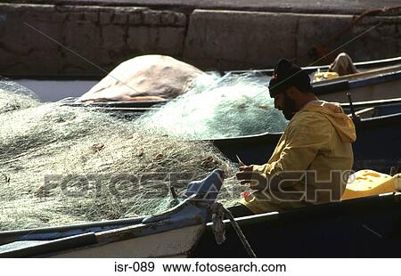 Stock Photo - Man Mending Fishing Nets on Quayside Akko Israel. Fotosearch