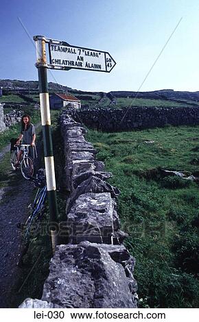 Stock Image - Woman with a Bike by a Signpost Ireland. Fotosearch
