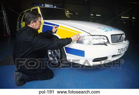 Stock Image - Mechanic Sticking Stripe onto Police Patrol Car UK. Fotosearch
