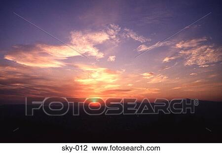 Stock Image - Altocumulus Clouds against a Setting Sun. Fotosearch