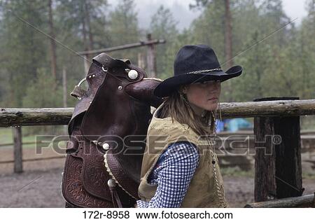 Stock Photo - fence, woman, hat, western, outdoors, carrying. Fotosearch