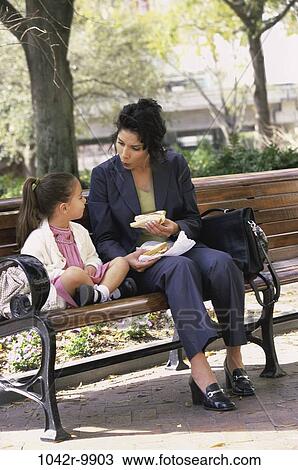 Stock Image - people, eating, bench, mother, Hispanic, outdoors, park. Fotosearch