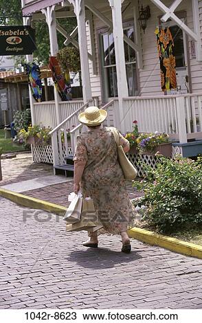 Stock Image - people, woman, hat, walking, outdoors, carrying, shopping. Fotosearch
